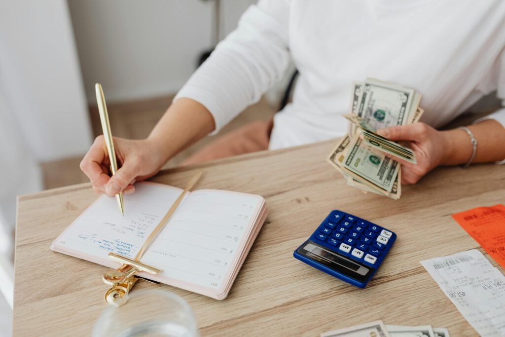 pexels-photo-5900184-5900184 Adult holding cash and writing in planner while using a calculator at home.