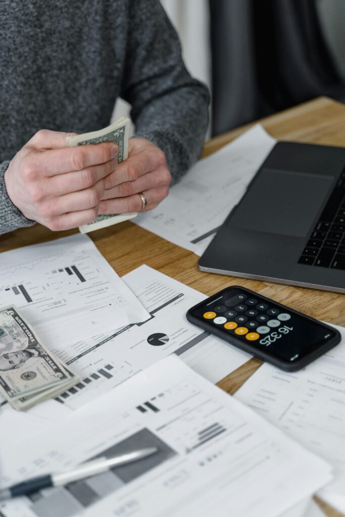 pexels-photo-6694485-6694485 Hands counting money at a workspace with a laptop, calculator, and financial documents.