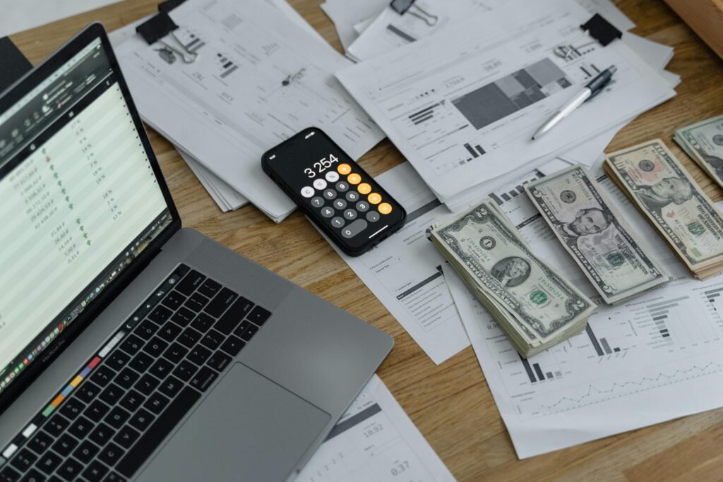 pexels-photo-6694543-6694543 A desk with financial documents, currency, a laptop, and phone calculator.