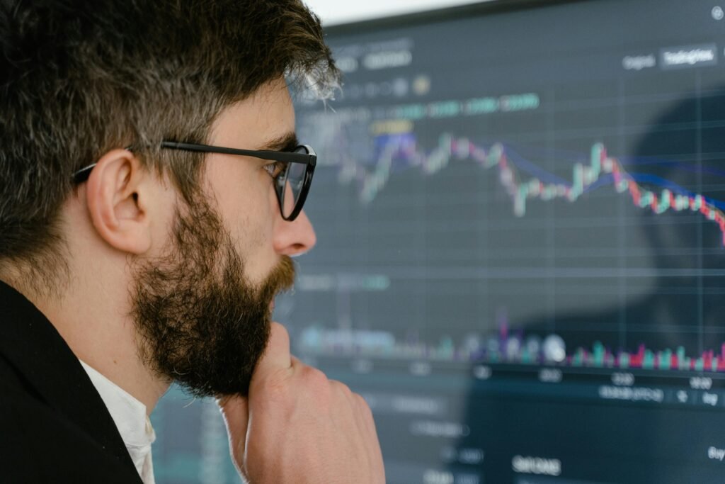 pexels-photo-7567235-7567235 A focused man with glasses studies stock market graphs on a screen, pondering insights.