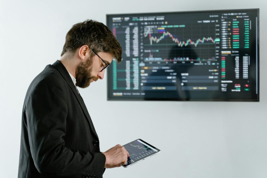 pexels-photo-7567525-7567525 Professional man using tablet in front of cryptocurrency trading screen indoors.
