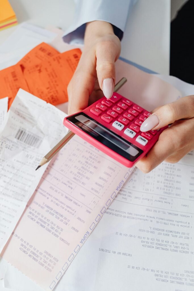 pexels-photo-7680692-7680692 Hands using a red calculator surrounded by financial documents and receipts, symbolizing financial management.