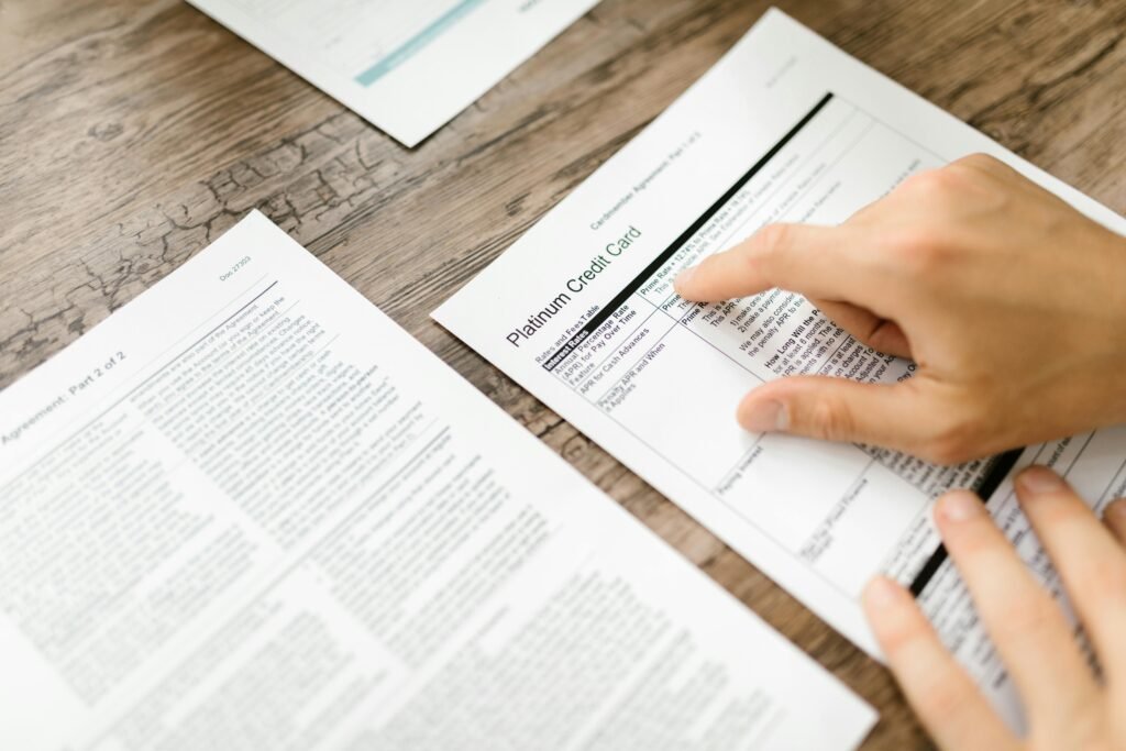 pexels-photo-7821905-7821905 A hand examining a credit card agreement on a wooden desk, highlighting financial review.