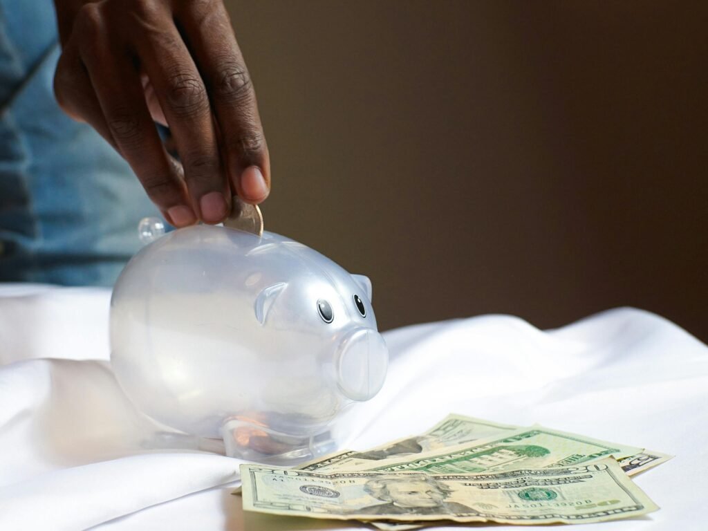 pexels-photo-3848193-3848193 A hand placing a coin in a piggy bank with dollar bills nearby signifying savings and finance.