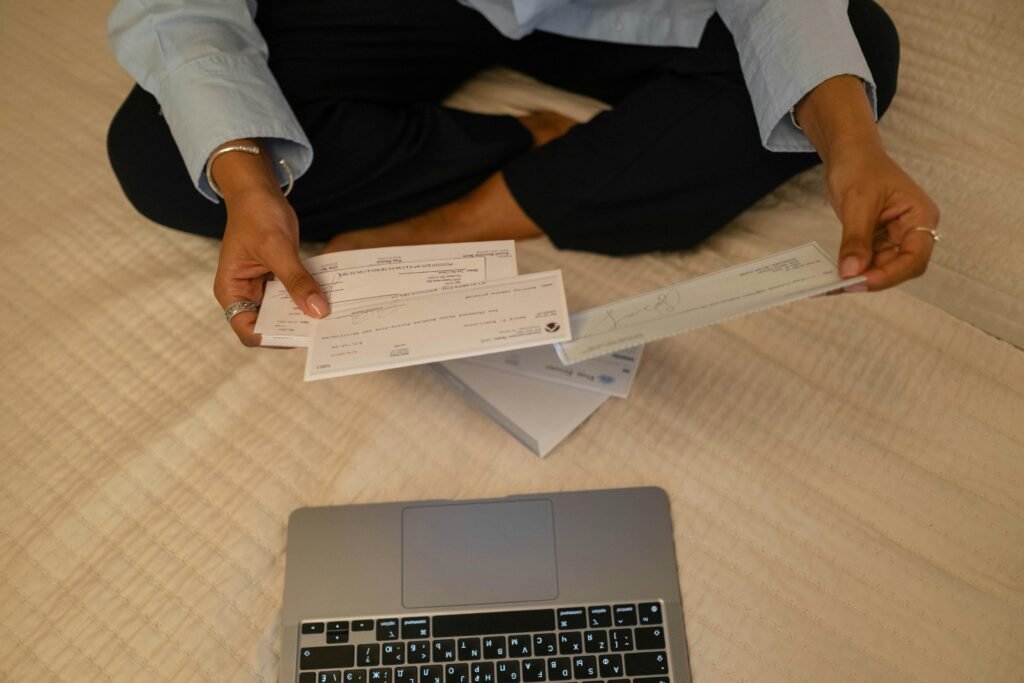 pexels-photo-6862443-6862443 Close-up of hands holding cheques beside a laptop indoors for financial tasks.