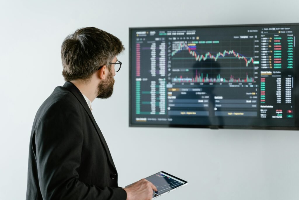 pexels-photo-7567561-7567561 Man observing stock market data on a screen and holding a tablet, representing financial analysis and trading.